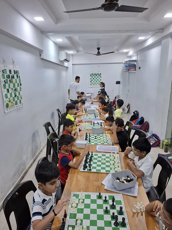Surat Chess Club's classroom on VIP Road, Vesu, with students at green boards and a demonstration board on the wall
