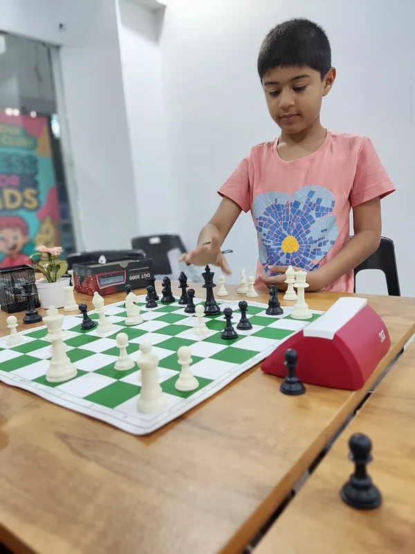 A boy setting up a chessboard next to a digital chess clock before a timed practice game in Surat