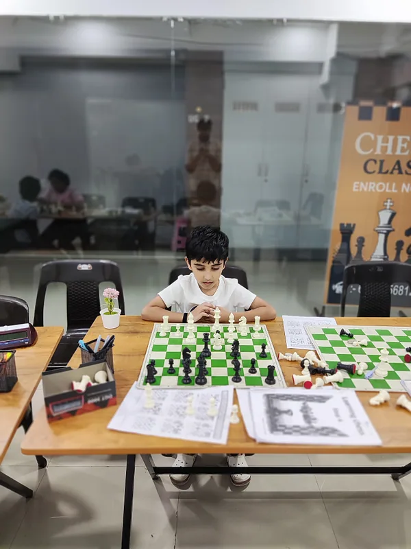 A student working through chess puzzle worksheets beside his board at Surat Chess Club