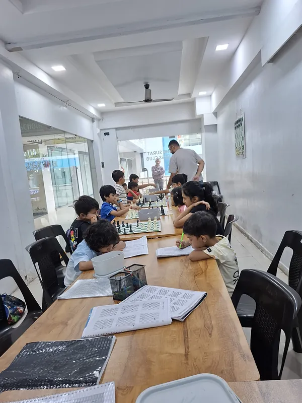 Students working through chess workbooks while the coach helps at a board, Surat Chess Club, Vesu