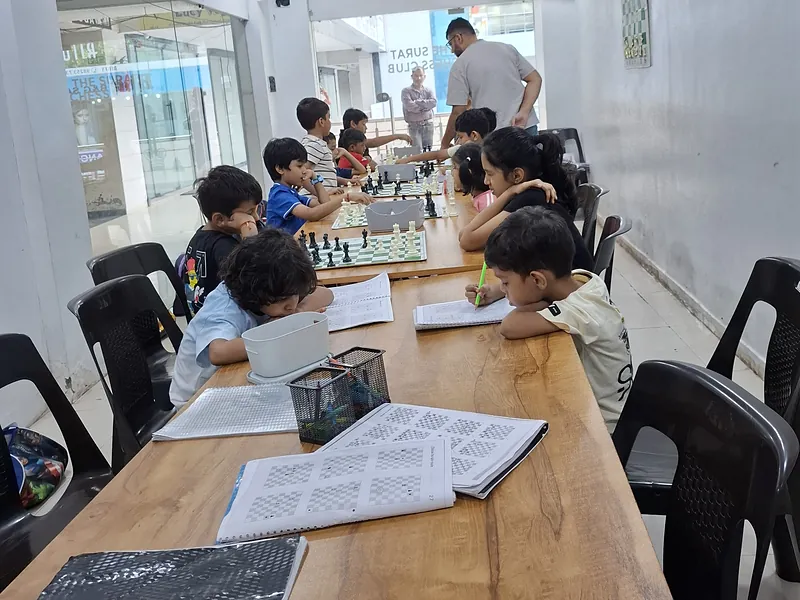 Students solving workbook positions while the coach checks a board at Surat Chess Club