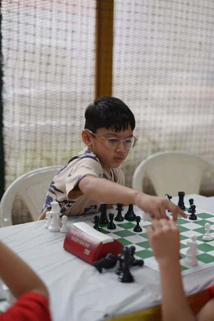 A boy in glasses reaching across the board to make his move